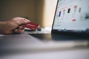 A hand holds a red loyalty card over a laptop displaying an online shopping website