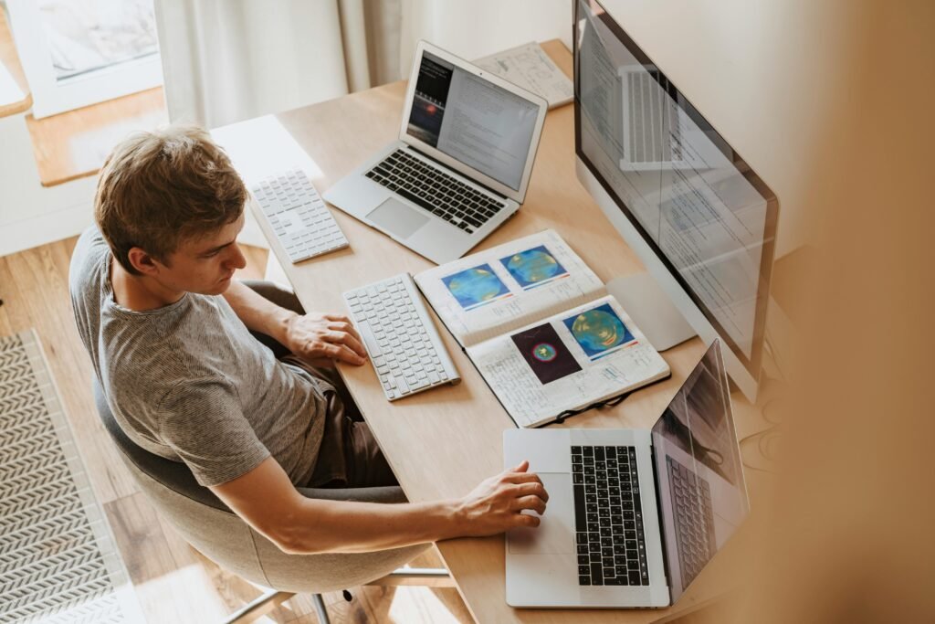 A man works at a desk with multiple laptops and a notebook, possibly researching WordPress productivity plugins