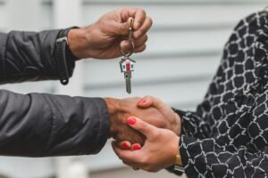Hands exchange a house-shaped key, symbolizing a real estate transaction